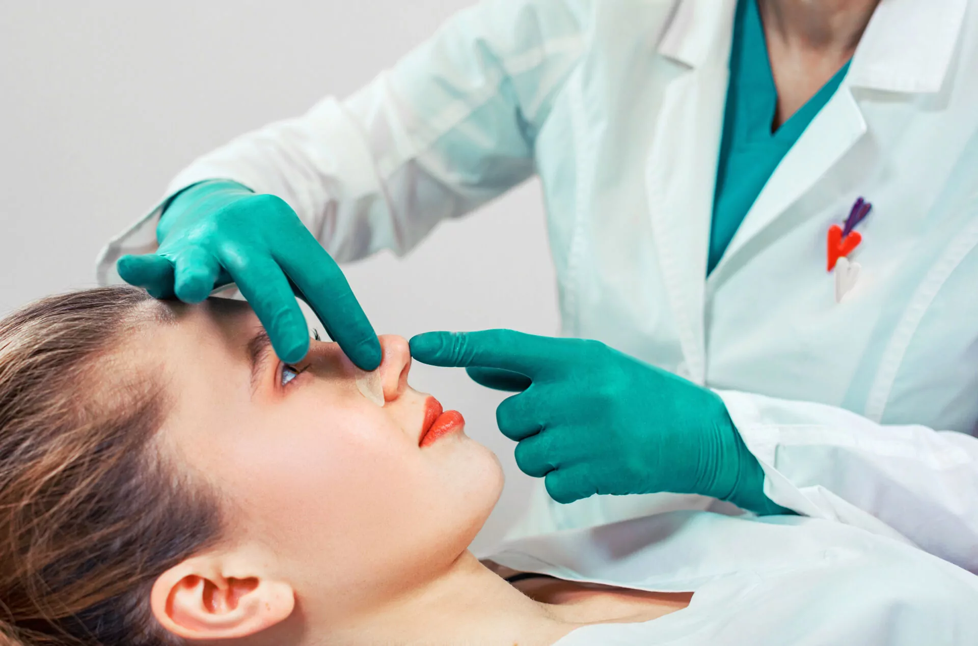 Rhinoplasty, the surgeon hands touches the patient s nose. People, cosmetology, plastic surgery and beauty concept – surgeon or cosmetologist hands touching female face. Rhinoplasty, the surgeon hands touches the patient s nose. People, cosmetology, plastic surgery and beauty concept – surgeon or cosmetologist hands touching female face.